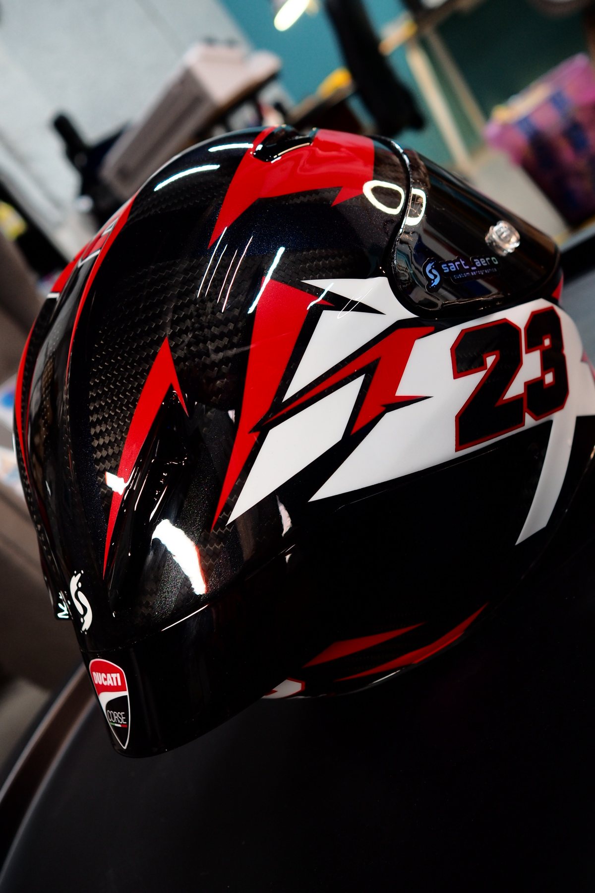 Front three-quarter of the Ducati #23 helmet showing the white 23 over red and black lightning panels