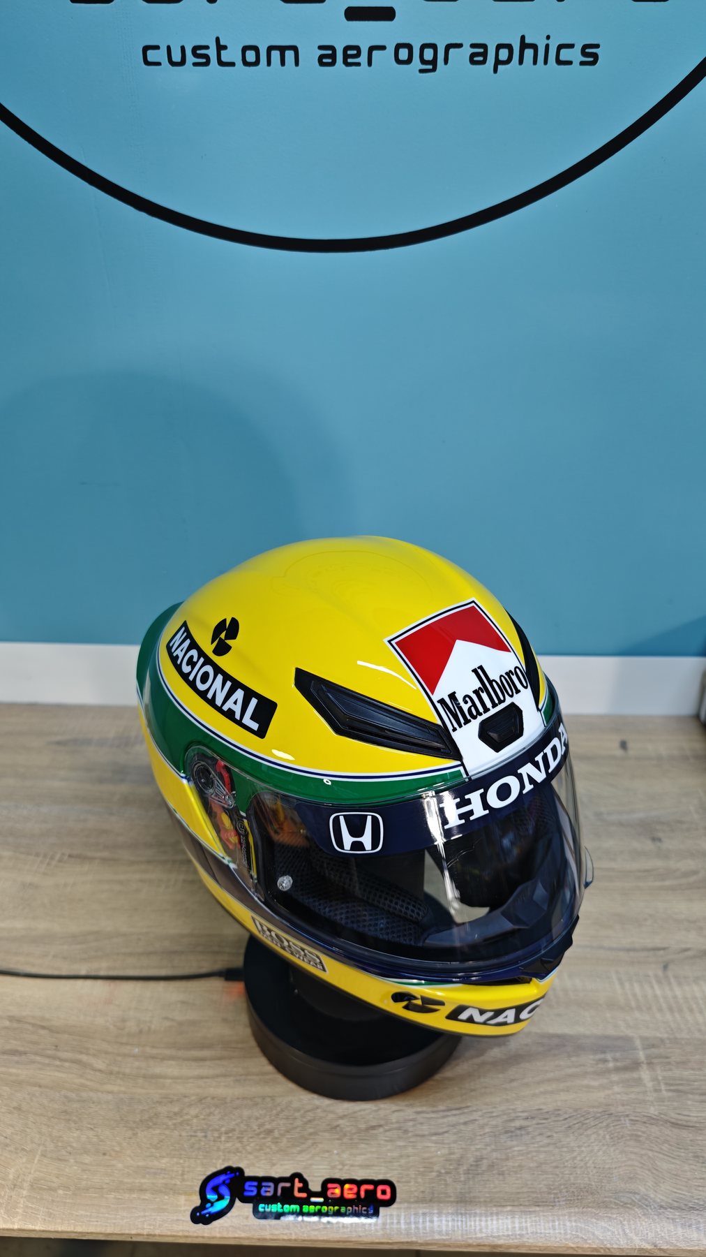 The helmet on a wooden bench against a pale blue wall, showing the green and blue lower band